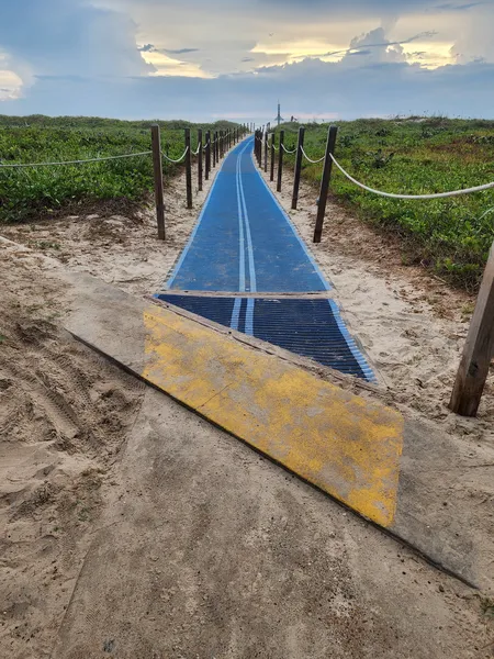 A blue Mobi-mat runs from a wooden ramp between rope fences over the dunes toward the Gulf.