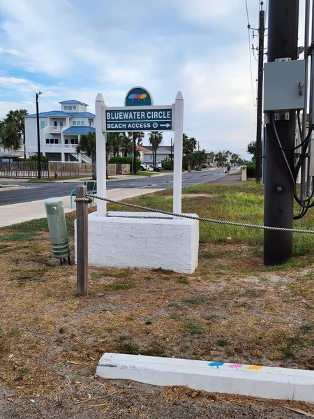 The Bluewater Circle Beach Access sign beside a rope-lined path, with beach houses behind it.