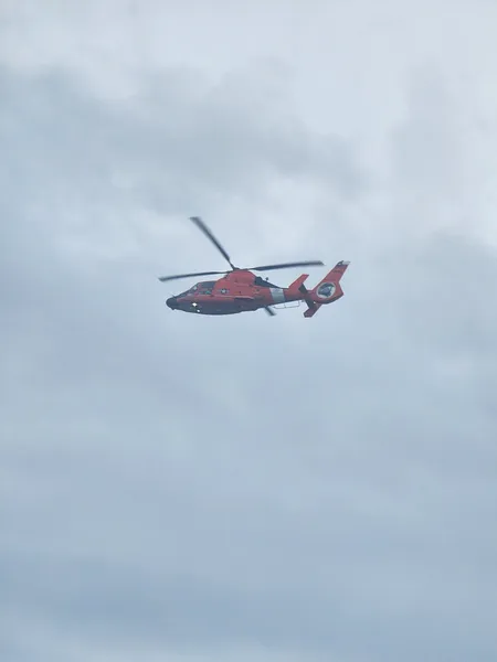 An orange-and-white U.S. Coast Guard helicopter in flight under a gray sky.