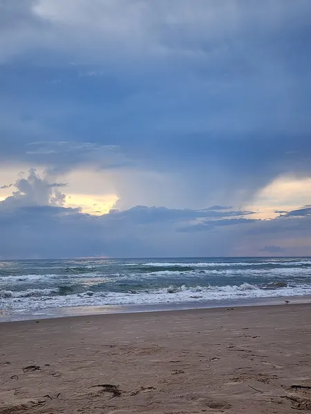 Tall gray clouds with a gap of pale light over the Gulf and a low line of surf.