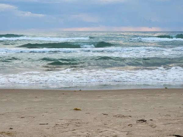 Rows of green-gray Gulf waves breaking onto wet sand under a cloudy sky.