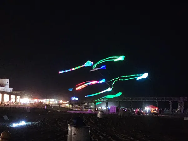 Several LED kites trail light across the night sky above the sand.