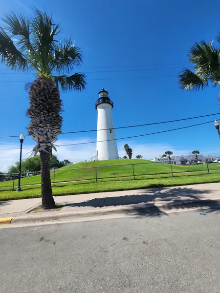 The white Port Isabel Lighthouse on its grassy hill between two palm trees under a deep blue sky.
