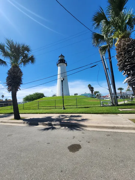 The Port Isabel Lighthouse seen from across the street, with palm trees along the curb.