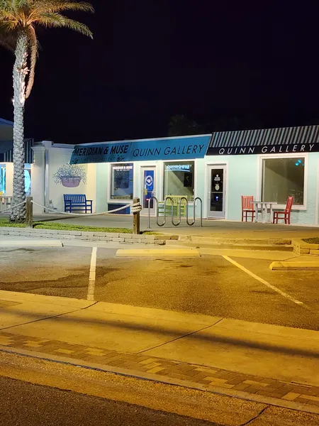 The Quinn Gallery storefront at night, with a blue bench and two red chairs out front.