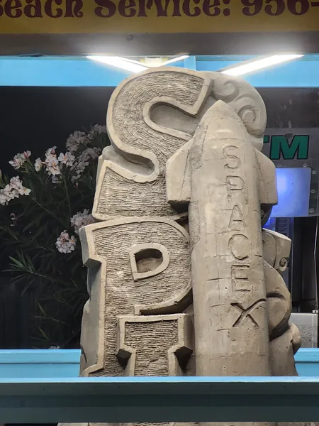 A sand sculpture of the letters SPI beside a rocket carved with the word SpaceX, in a lit booth.