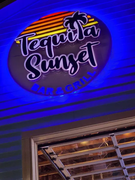 The Tequila Sunset Bar & Grill sign glowing under blue light at night.