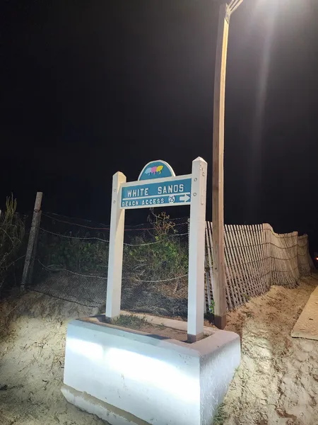 The White Sands beach access sign lit by a street lamp at night.