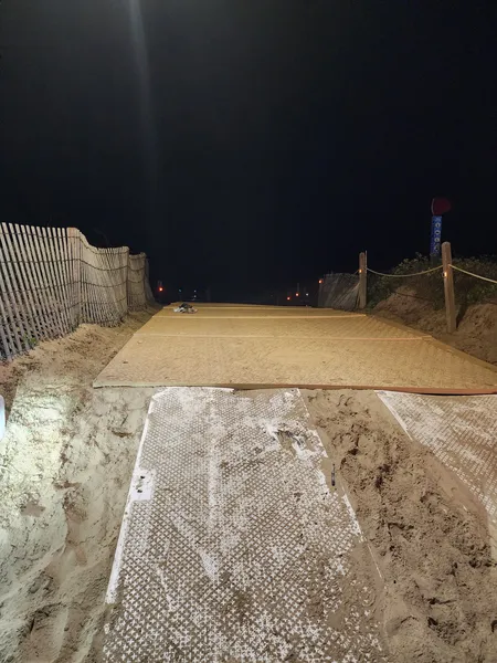 A Mobi-mat and a wooden ramp lead between sand fences toward the beach at night.