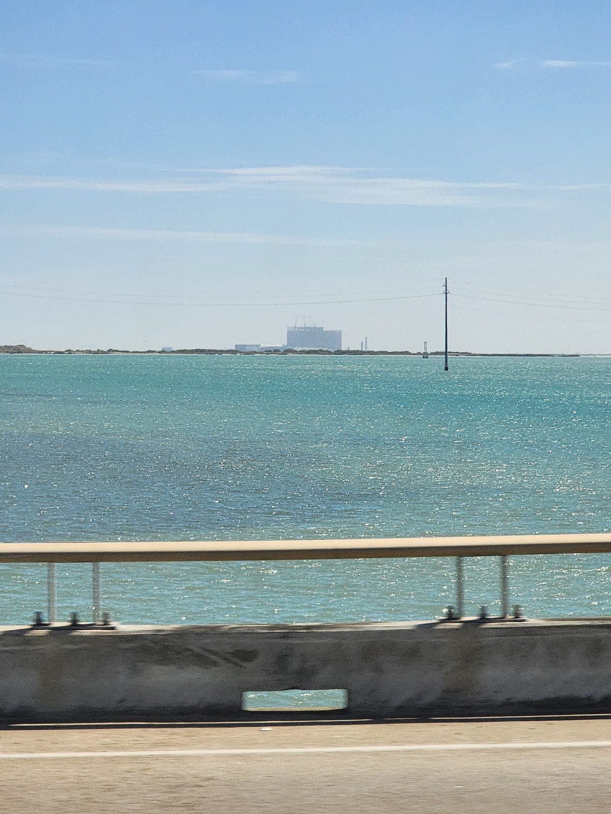 Blue bay water seen beyond a causeway railing and a distant low shoreline.