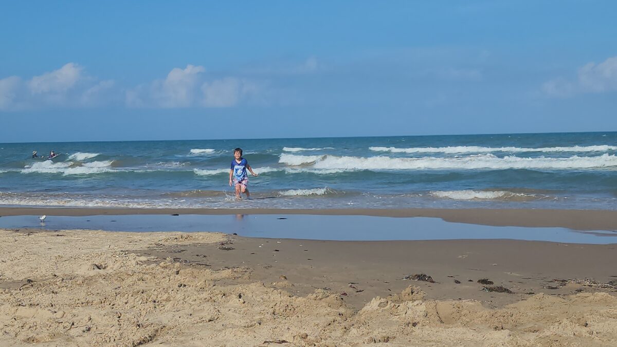 A child wades in gentle shallow surf near the shoreline.
