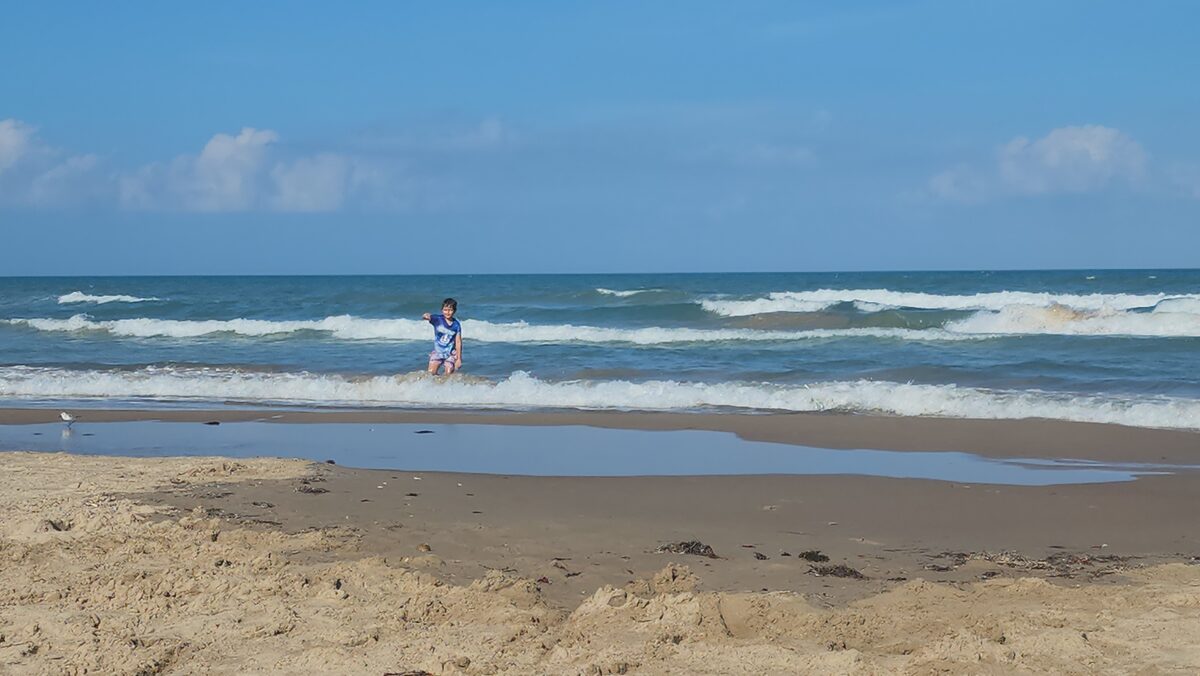 A child stands in shallow Gulf water as small whitecaps roll in.