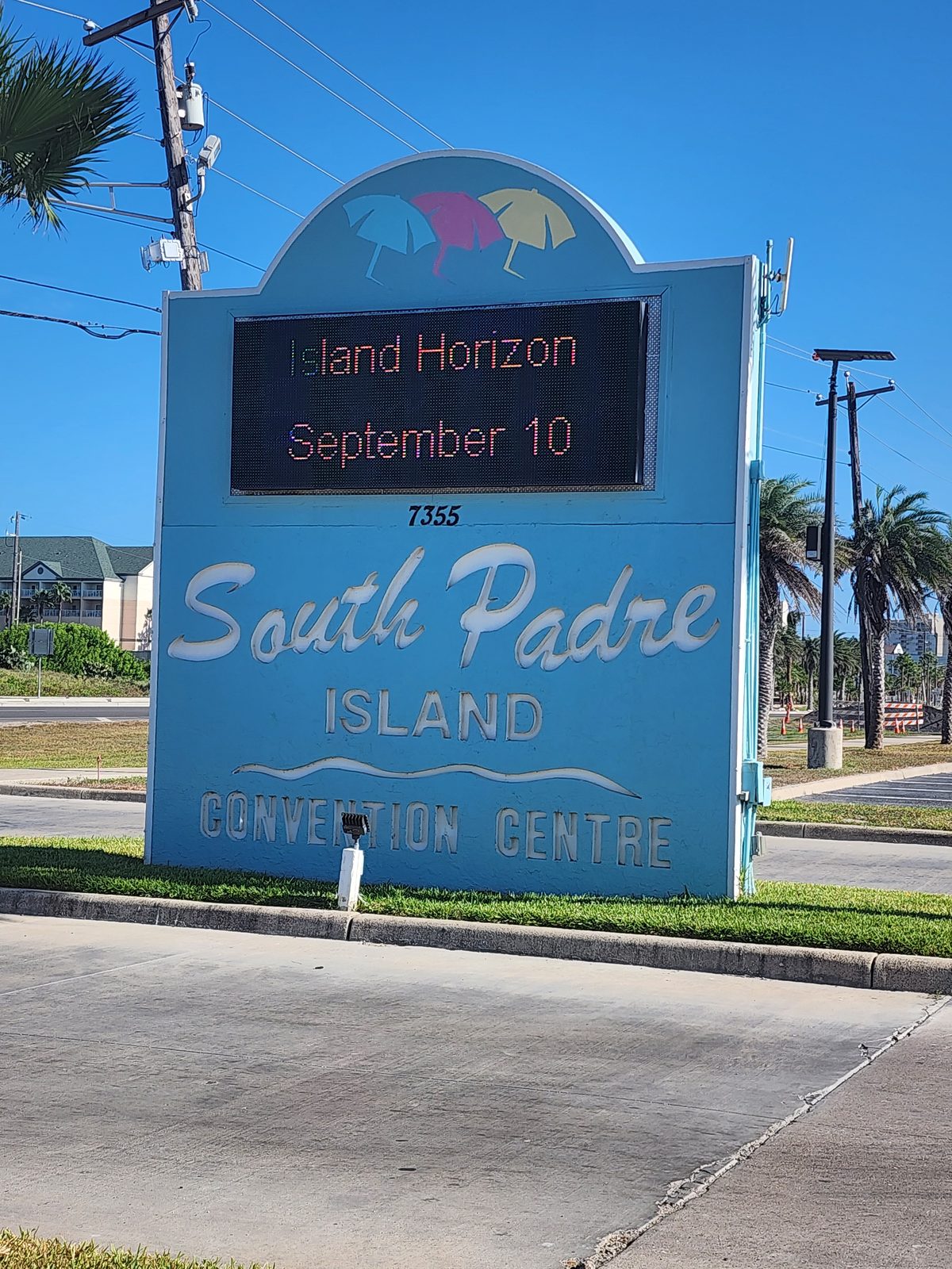 South Padre Island Convention Centre sign beside palms and a roadway.