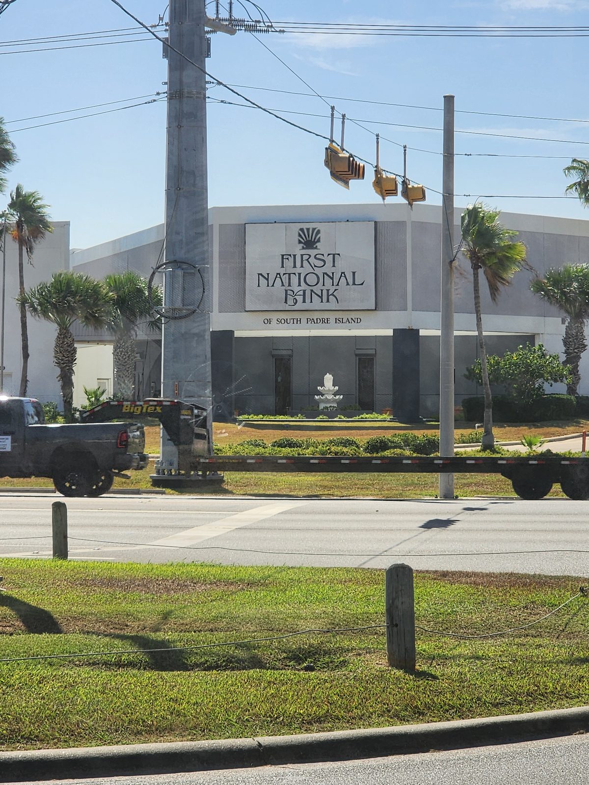 First National Bank building and palm trees viewed across a roadway.
