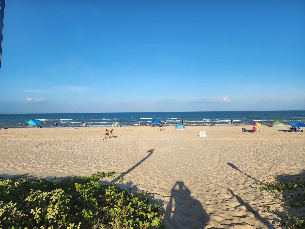 Distant visitors, colorful tents, and umbrellas spread across a broad Gulf beach.