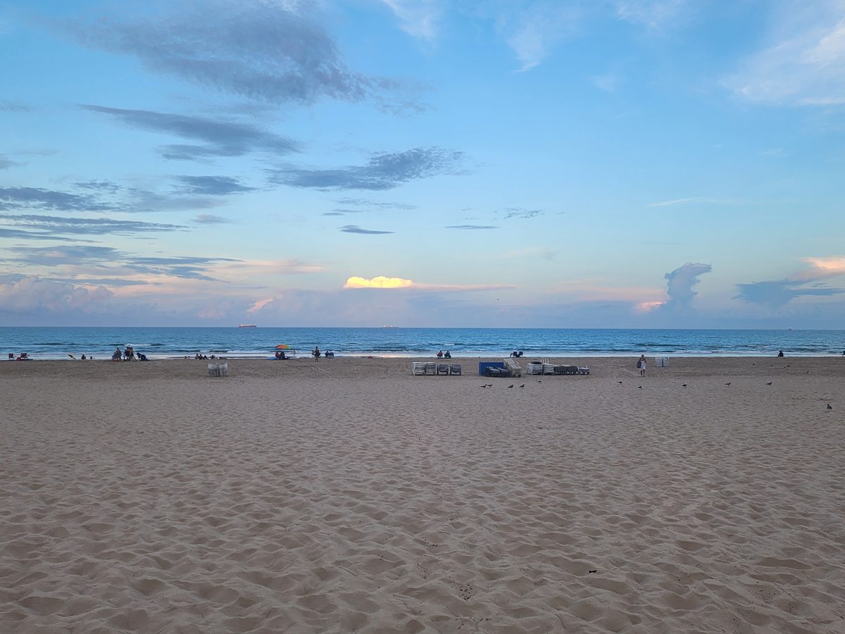 Wide sandy beach and distant beachgoers beneath a blue-and-gold sunset sky.