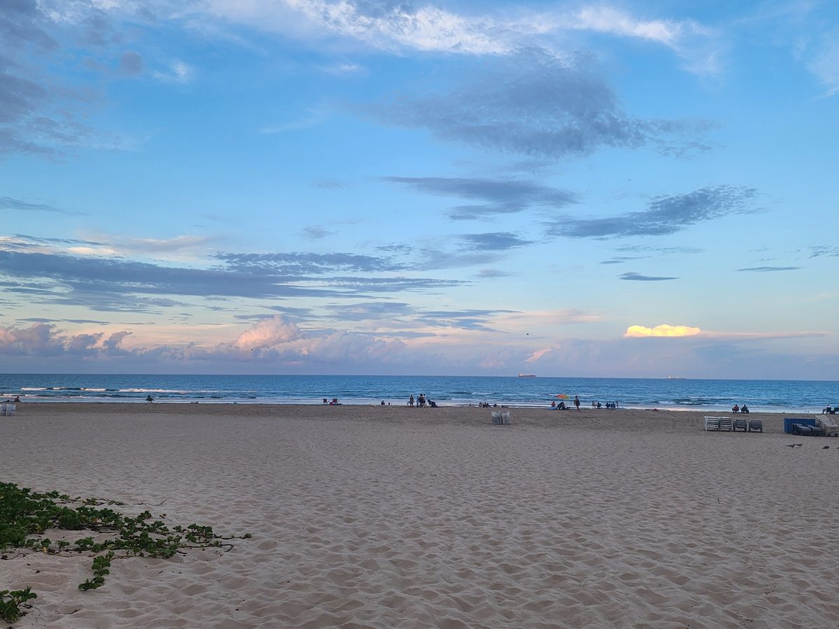 Beach chairs and small figures on a broad sandy beach beneath a sunset sky.