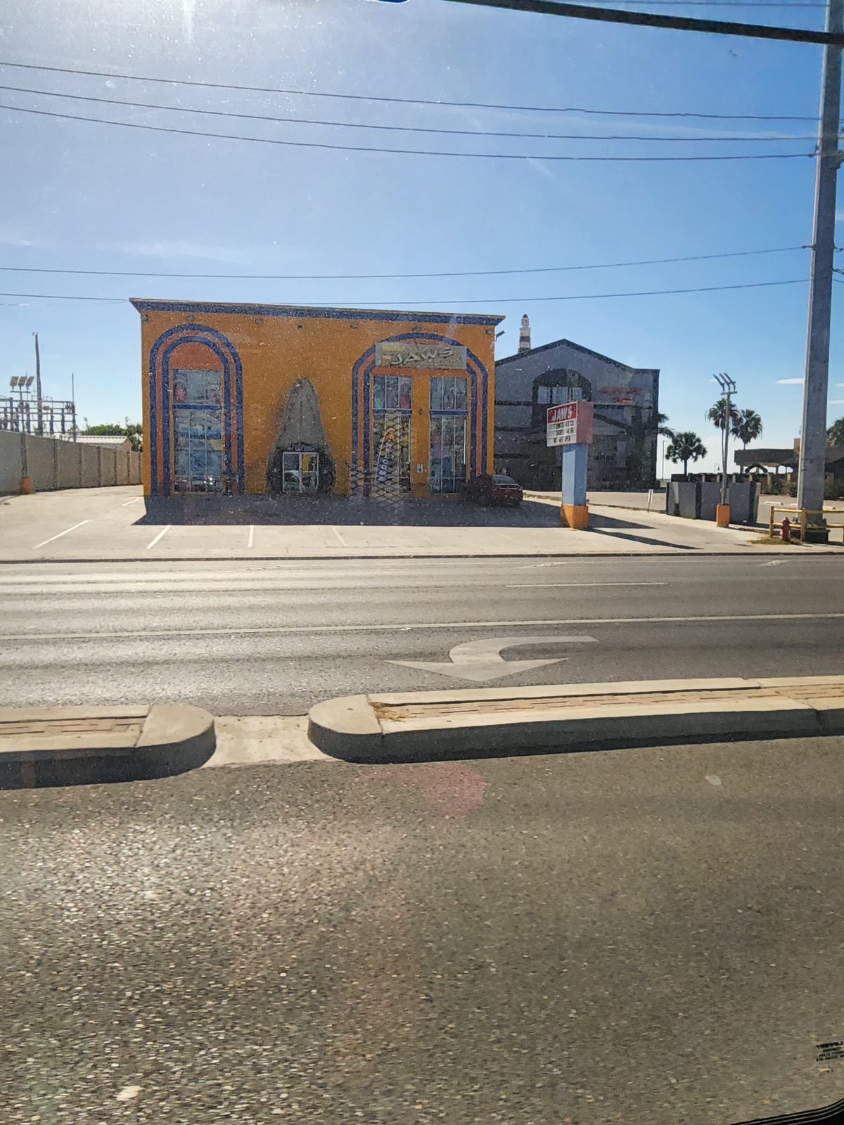 Bright orange shop with two tall arched glass storefronts in blue banding and JAWS lettering, behind a near-empty parking lot across a wide road.