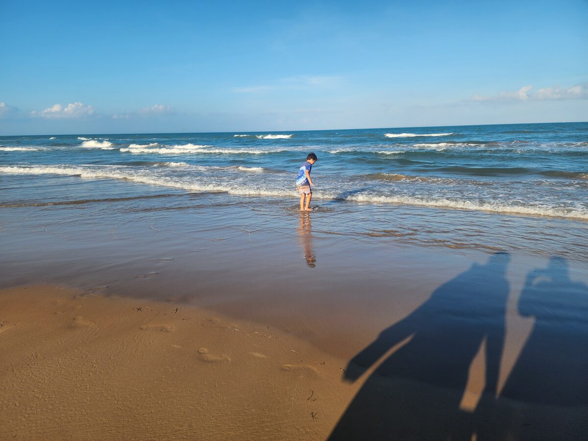 A child stands in shallow Gulf surf near the shoreline.