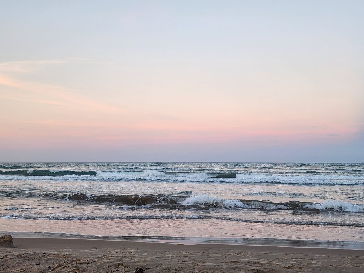 A pink dusk sky over rolling Gulf surf, its color reflected in the wet sand at the water's edge.