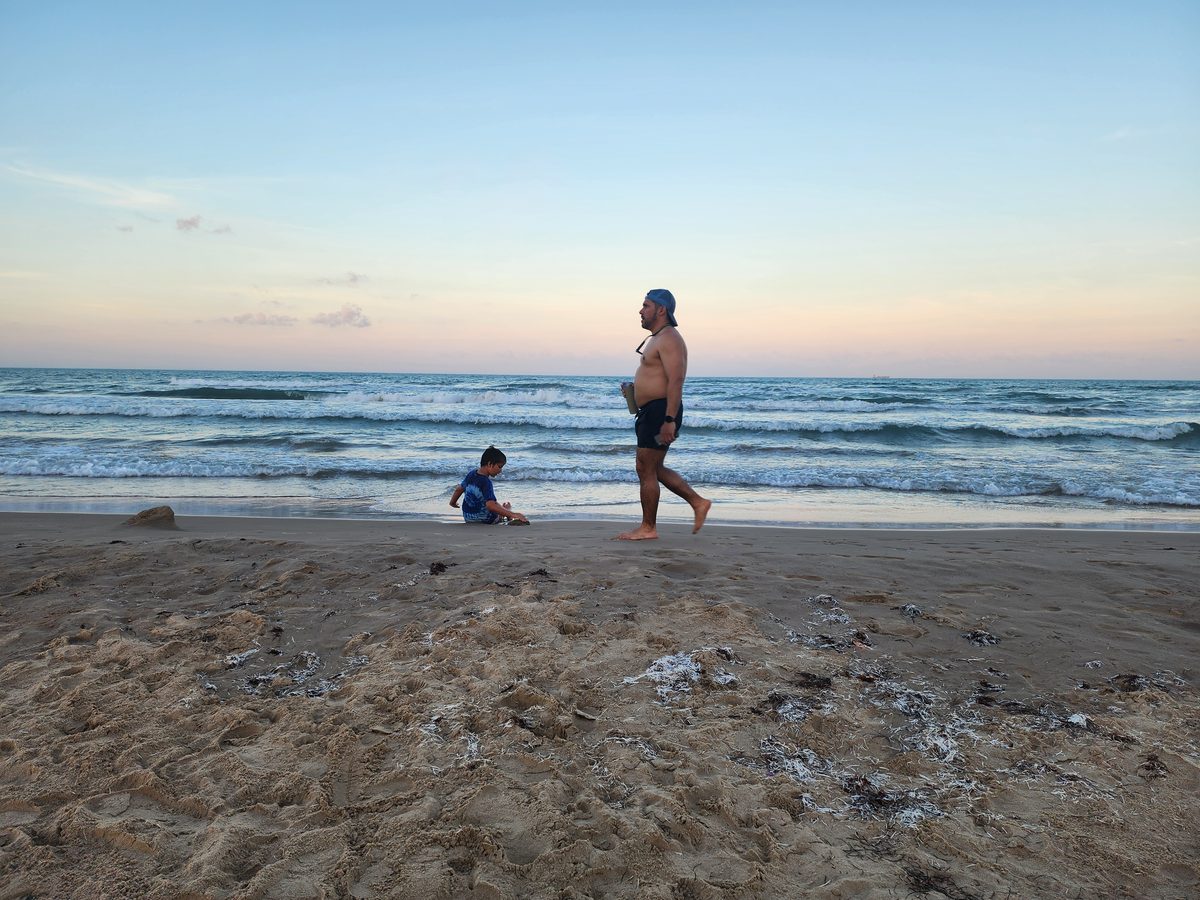 An adult and child near the shoreline in the last light of the day.