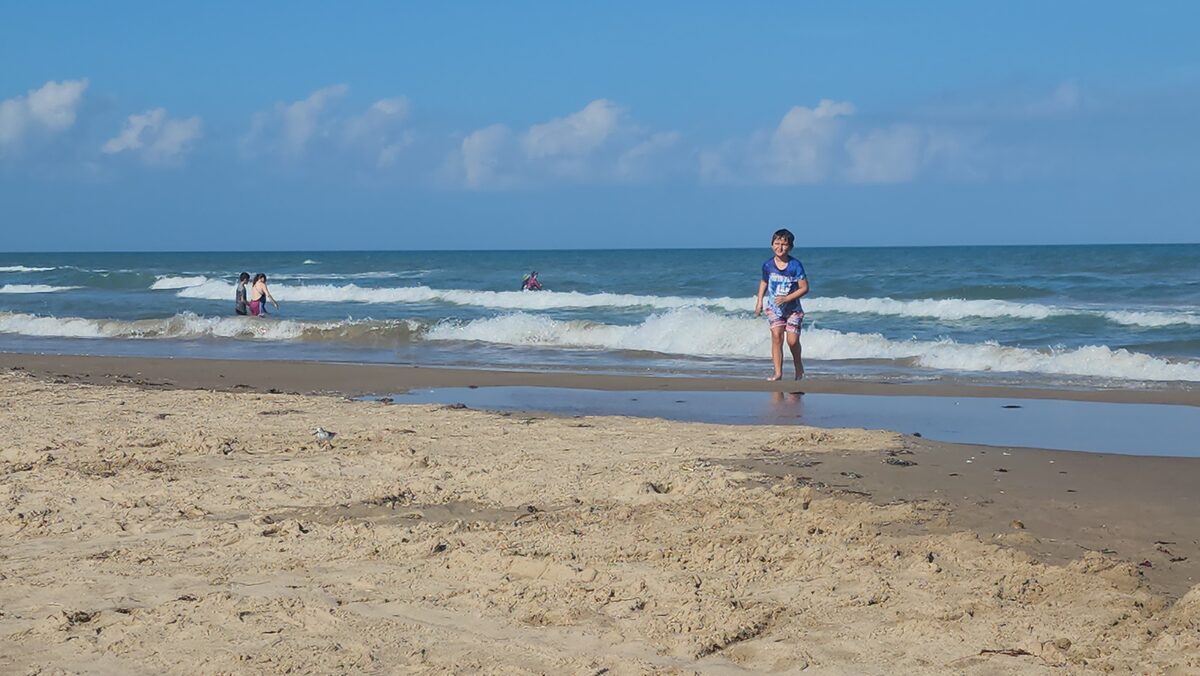A child and distant visitors wade in shallow Gulf surf.