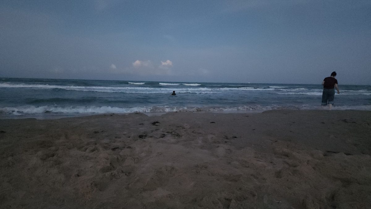 Dusk view of a wide sandy Gulf beach, with a swimmer's head visible in the surf and another person standing at the water's edge.
