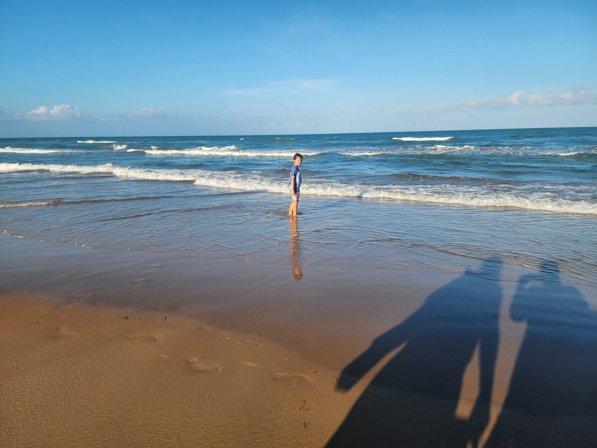 A child stands in shallow water at the Gulf shoreline in warm light.