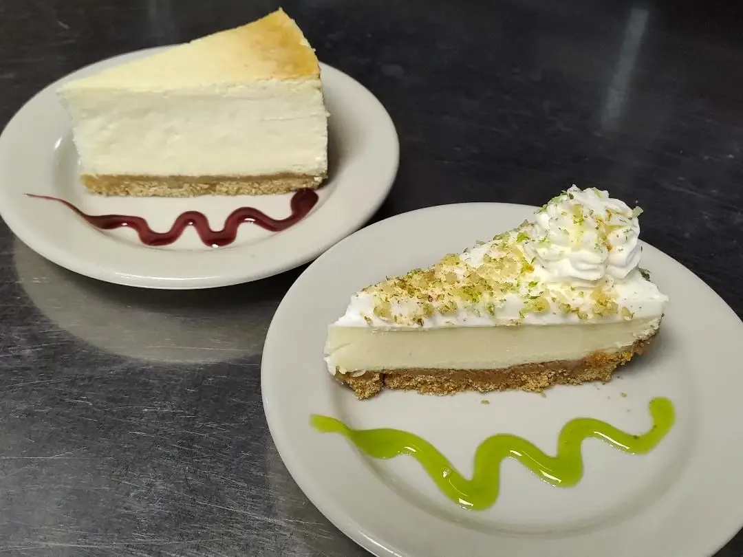A slice of New York cheesecake and a slice of key lime pie on white plates