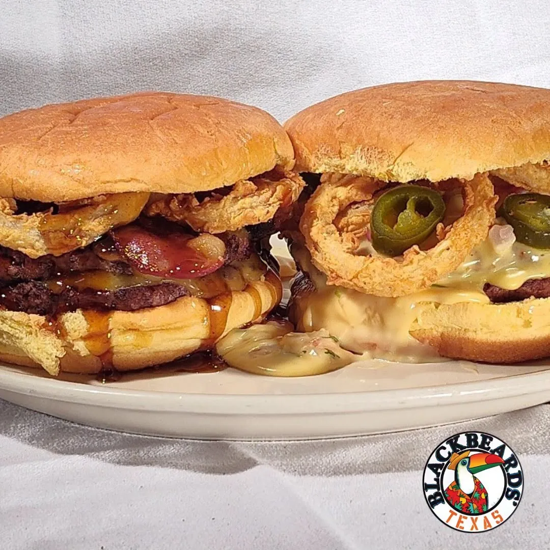 Two double-stacked burgers, one with bacon and fried onions, one with fried onions, jalapeños and queso