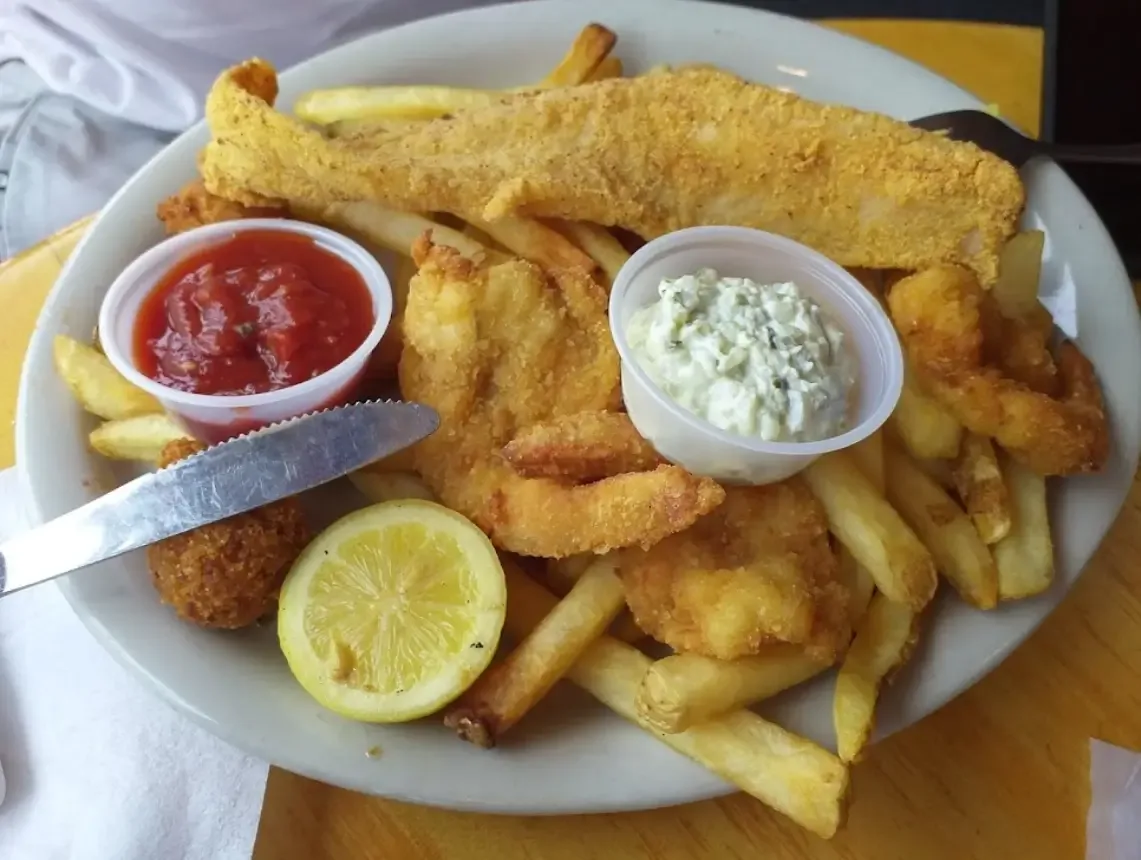 A fried fish fillet and fried shrimp with fries, hush puppies, tartar and cocktail sauce and a lemon