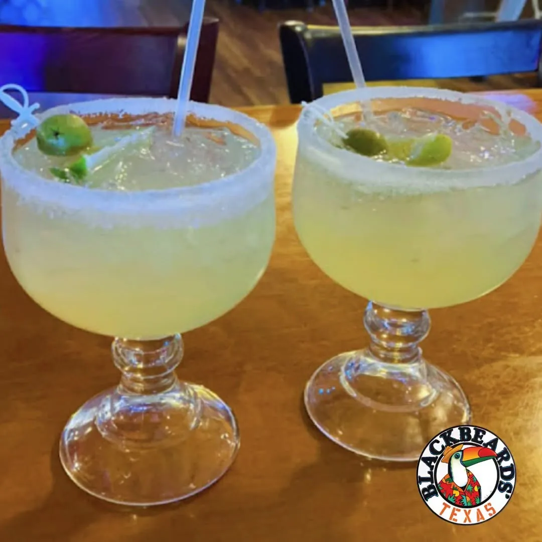 Two salt-rimmed margaritas with lime in stemmed glasses