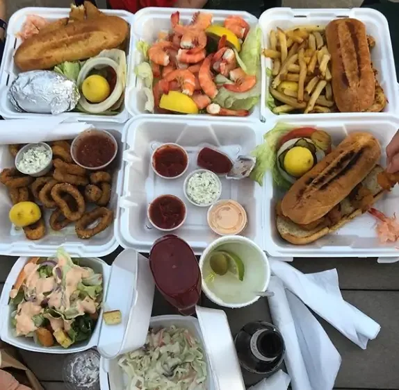 Takeout boxes of fried fish, shrimp cocktail, fries, calamari, a po’boy and salads