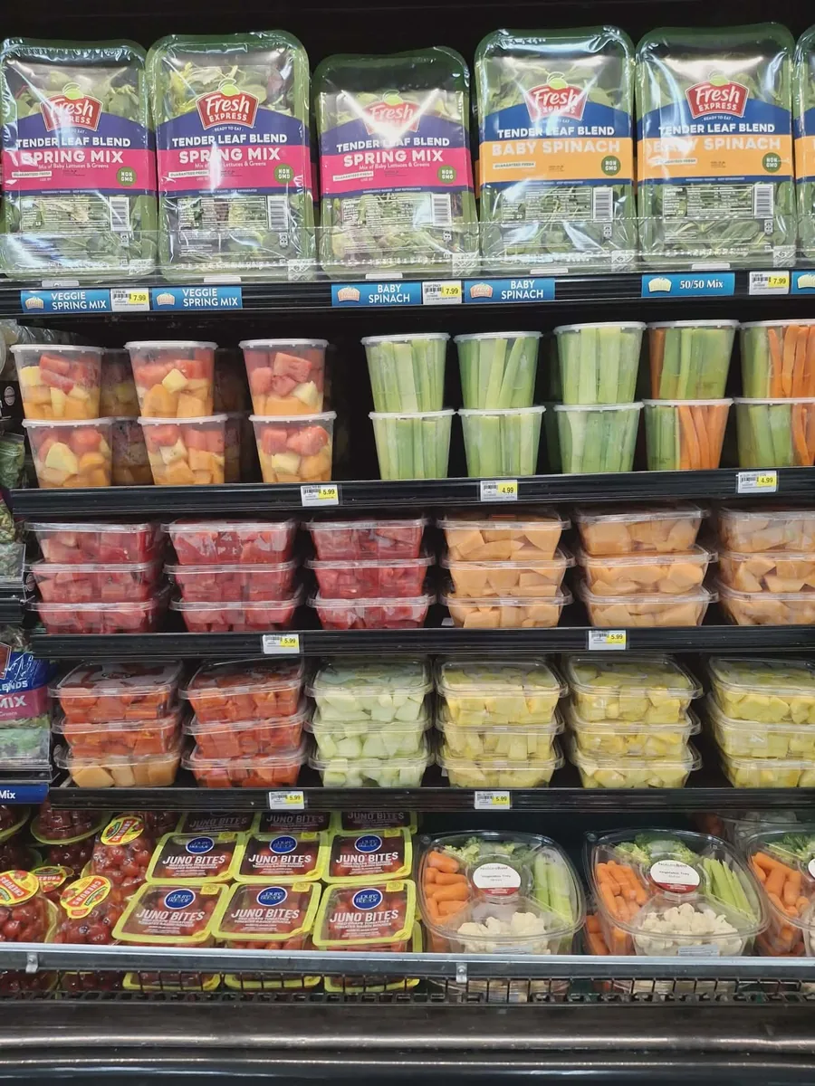 Shelves of cut fruit cups, celery and carrot sticks, veggie trays and bagged spring mix and baby spinach
