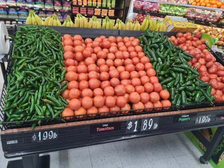 Bins of red tomatoes between piles of jalapeño and serrano peppers in the produce section