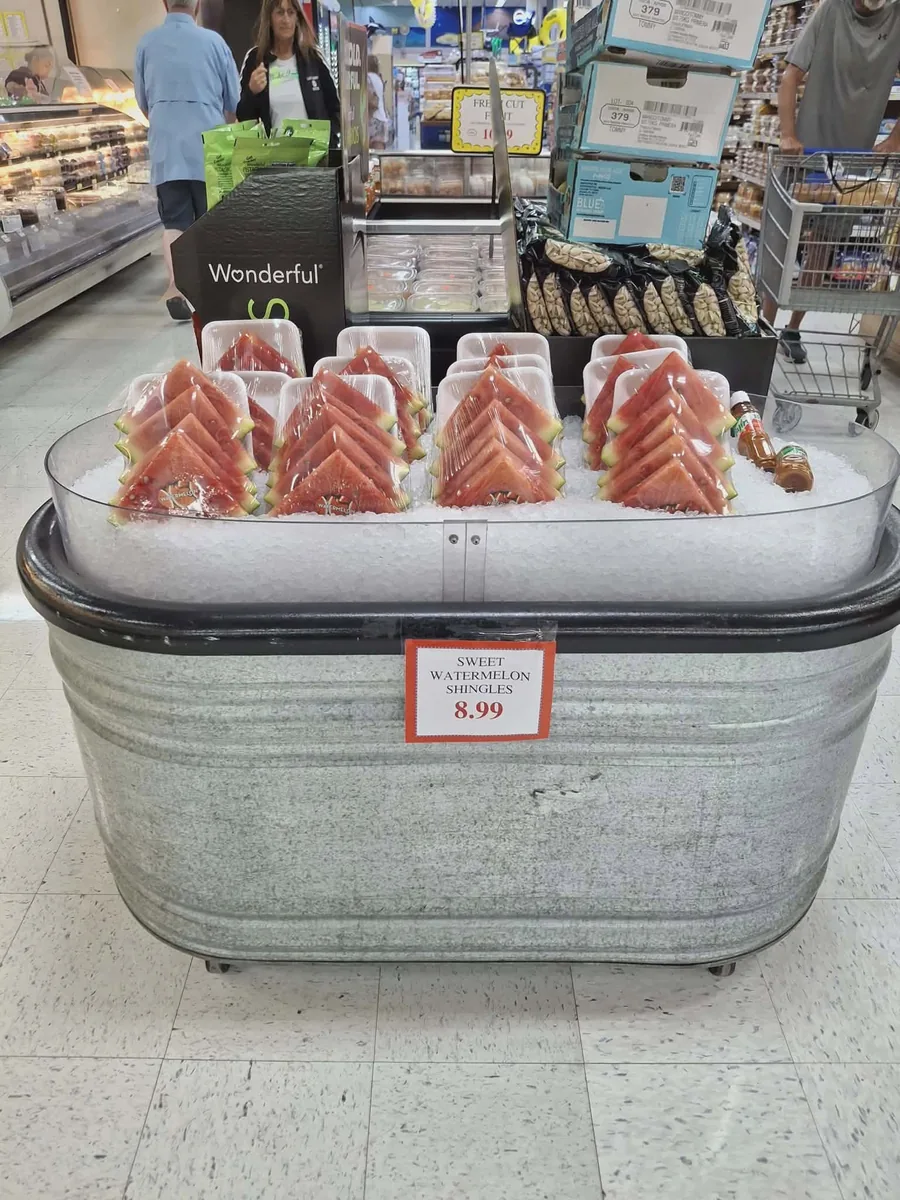 Wedges of sweet watermelon in clamshells on ice in a galvanized tub