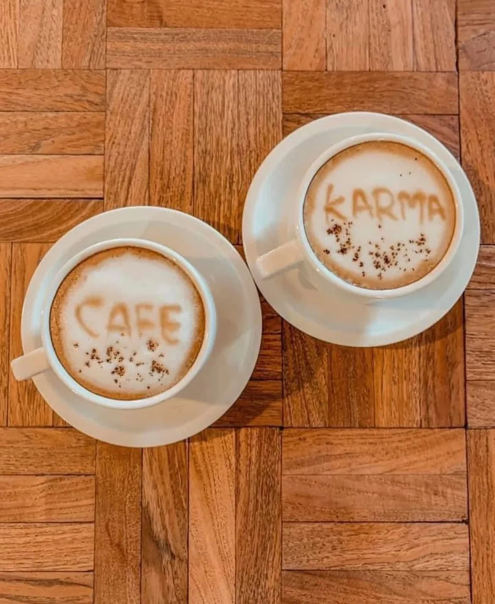 Two cappuccinos with "CAFE" and "KARMA" drawn in the foam on a parquet table