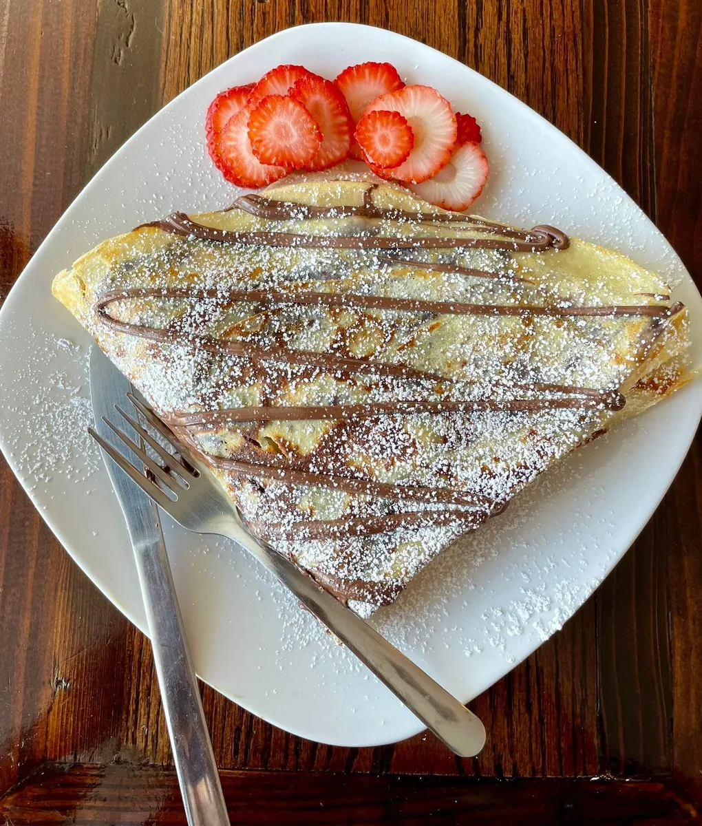 A folded crepe drizzled with chocolate and dusted with powdered sugar, with sliced strawberries