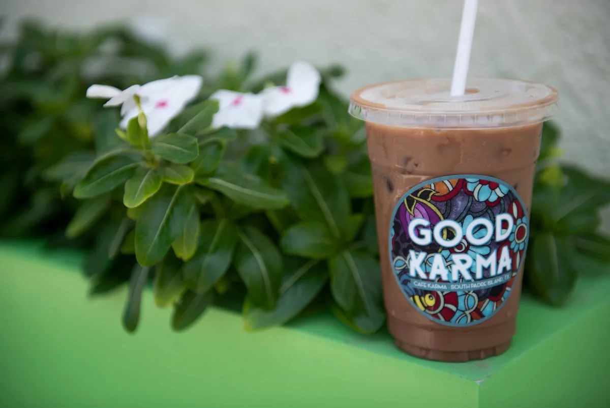 An iced coffee in a colorful "Good Karma" cup next to white flowers