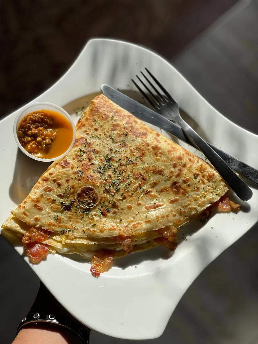A folded savory crepe filled with bacon, with a cup of salsa