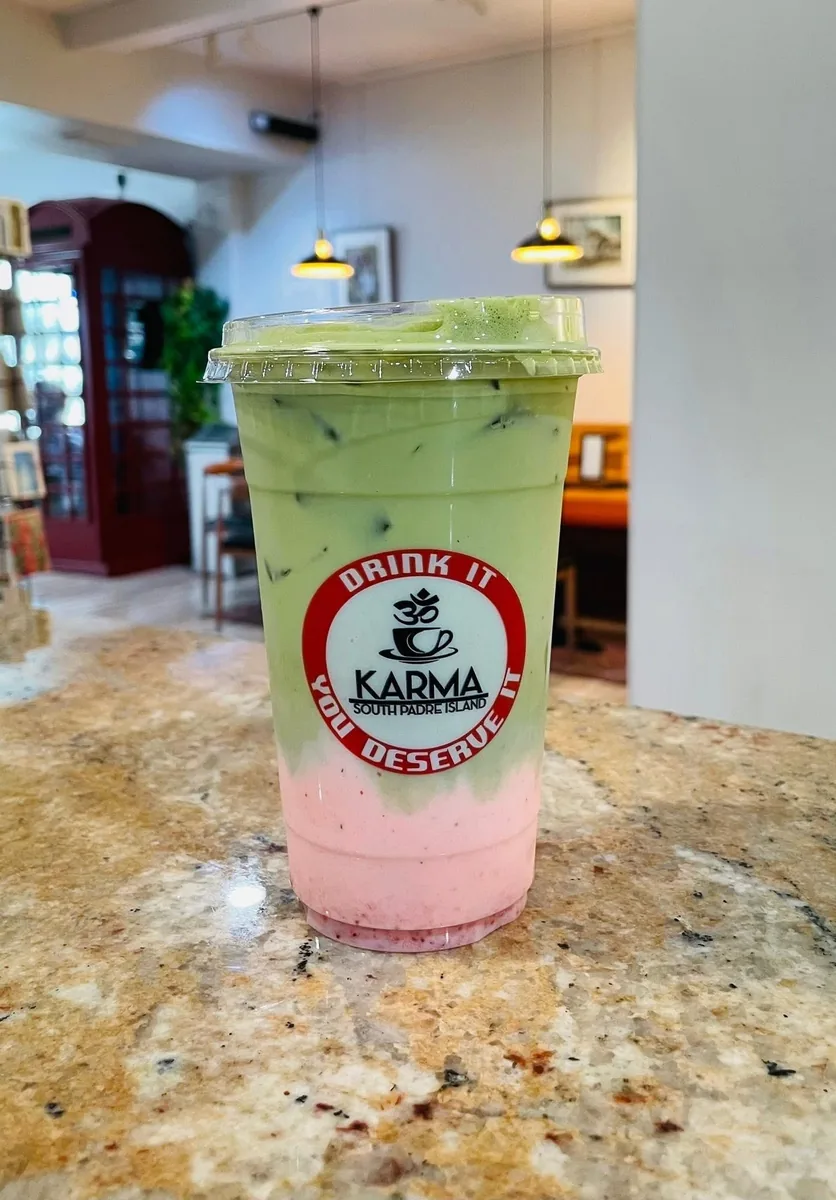 An iced strawberry matcha, pink below and green above, in a Karma "Drink it, you deserve it" cup on the counter