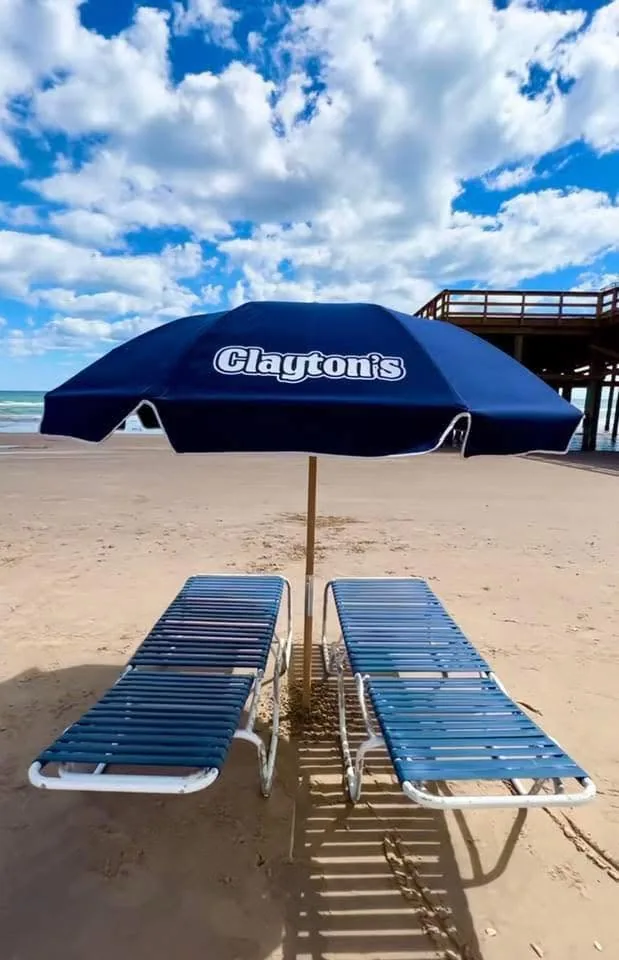A navy Clayton's umbrella over two blue loungers on the sand, with the pier behind