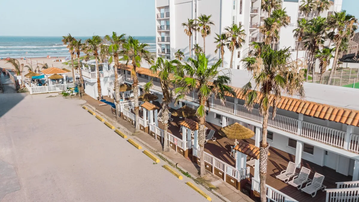Aerial view of the hotel's two-story buildings with palm trees and the beach and Gulf beyond