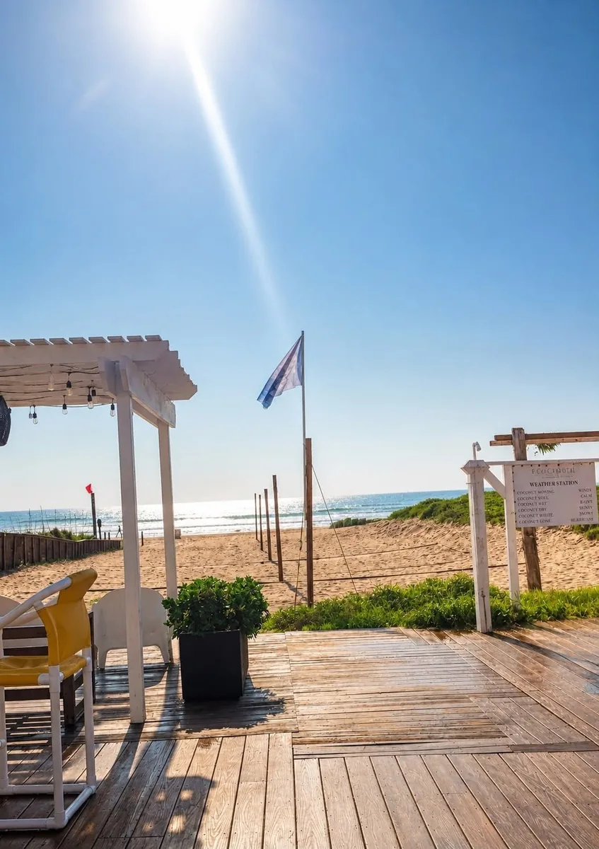 The wooden deck and pergola leading down to the beach, with a flag and the Gulf in the sun