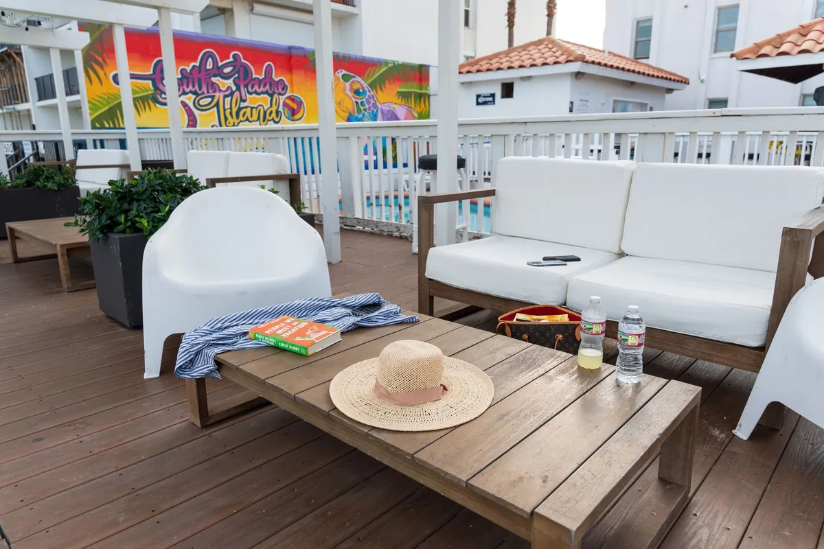 White lounge sofas and chairs around a wooden table on the deck, with a sun hat and a beach towel