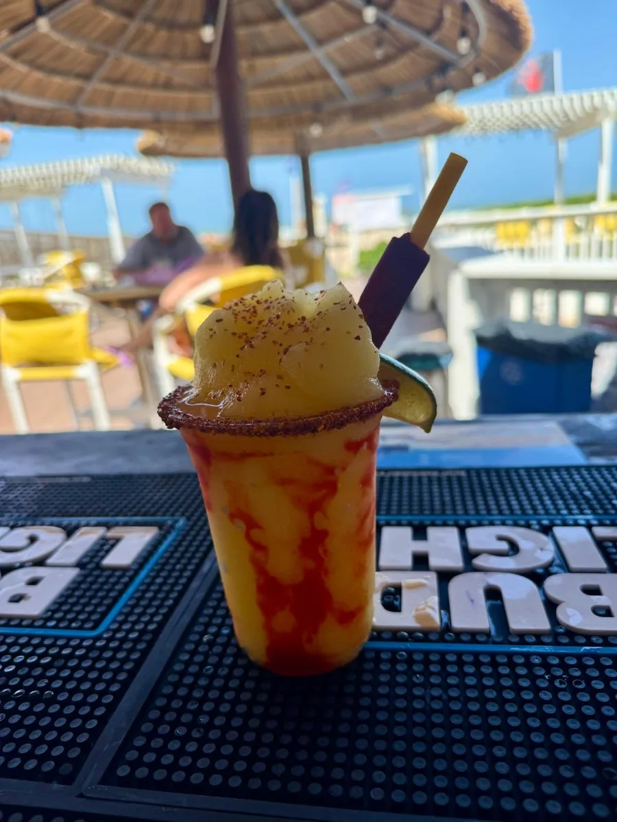 A frozen mango drink swirled with chamoy, with a chili-salt rim and a tamarind straw, on the bar