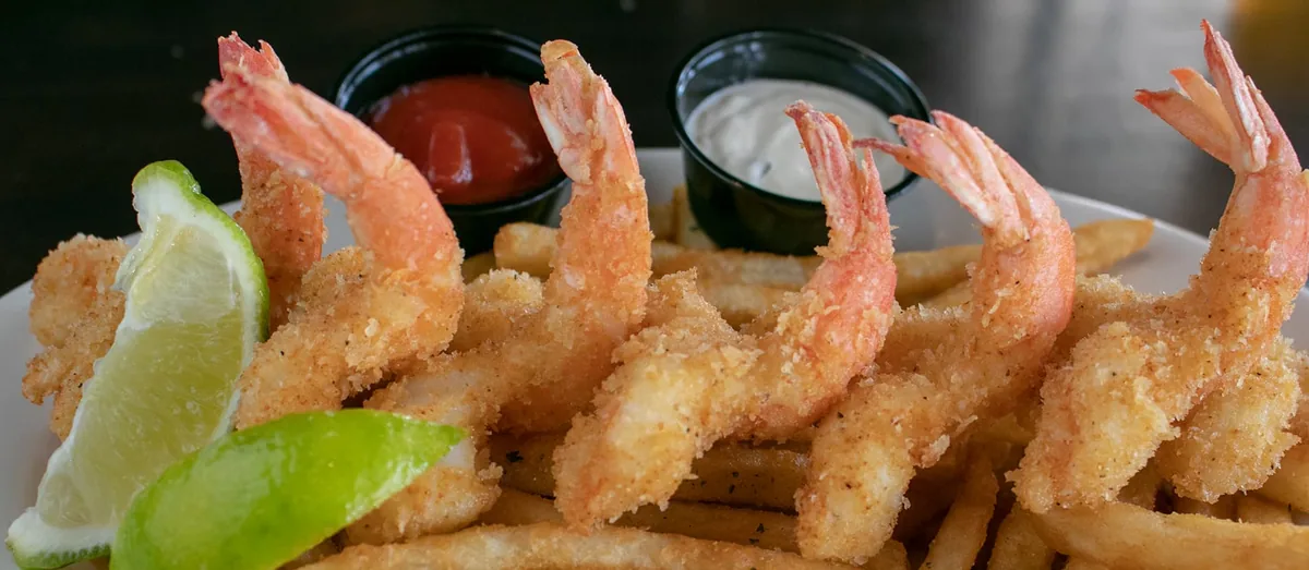 Golden fried shrimp on a bed of french fries with lime wedges, cocktail sauce and tartar sauce