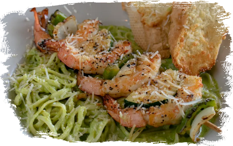 A grilled shrimp and vegetable skewer over pasta in a green sauce, topped with Parmesan, with garlic toast