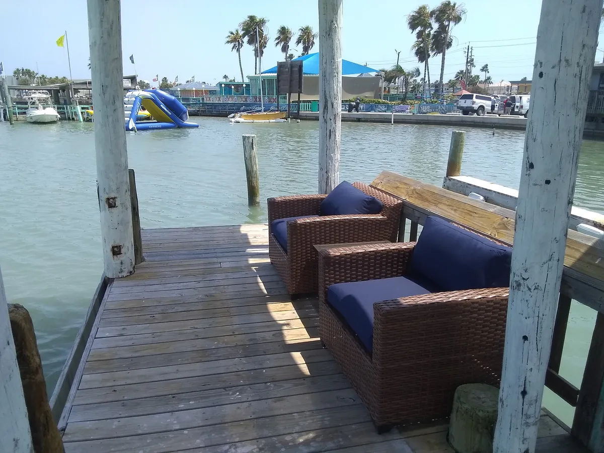 Wicker sofas with blue cushions on the dock facing the water, with a water slide in the distance