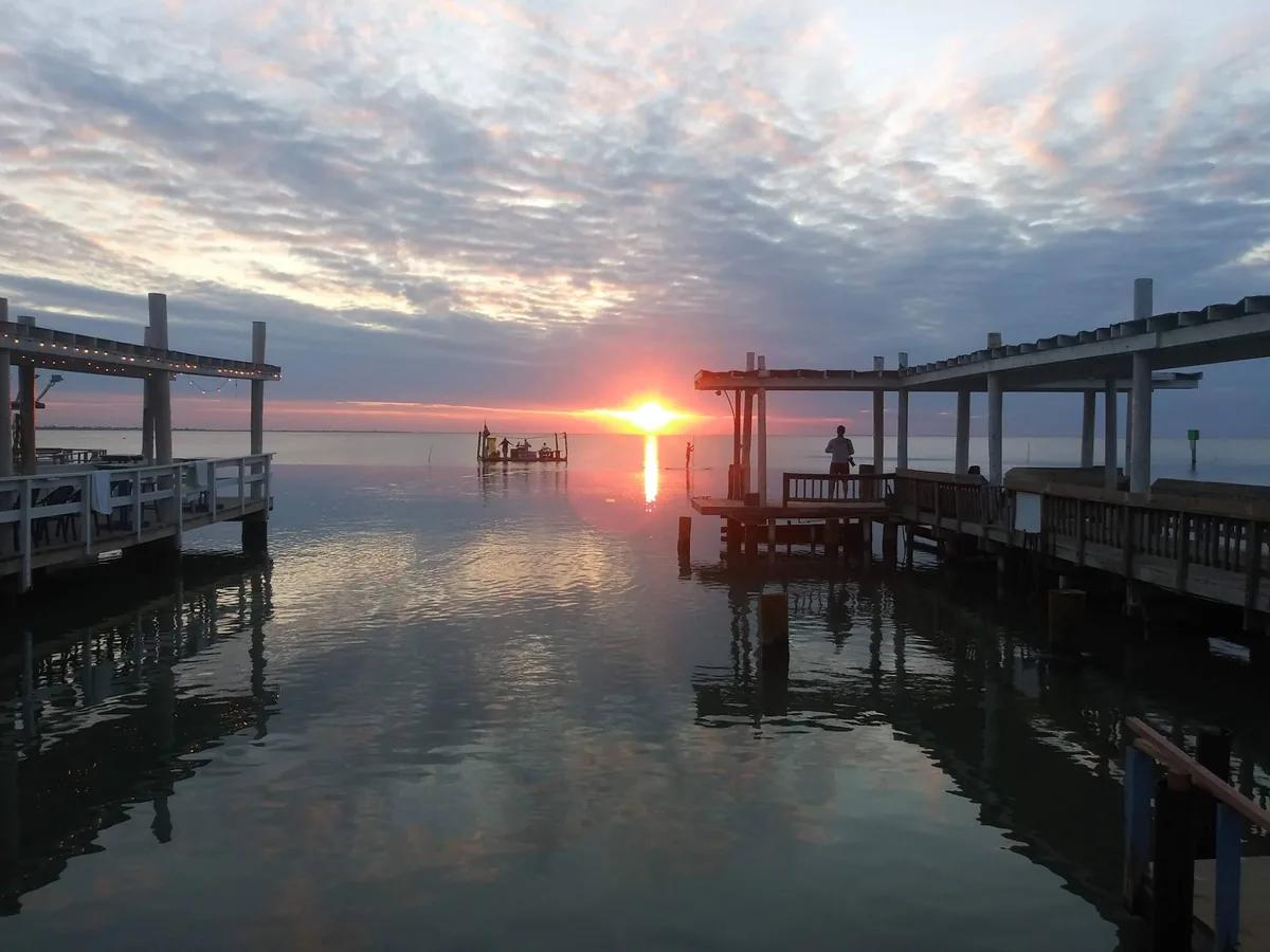 The sun setting over the bay between two piers, reflected in calm water